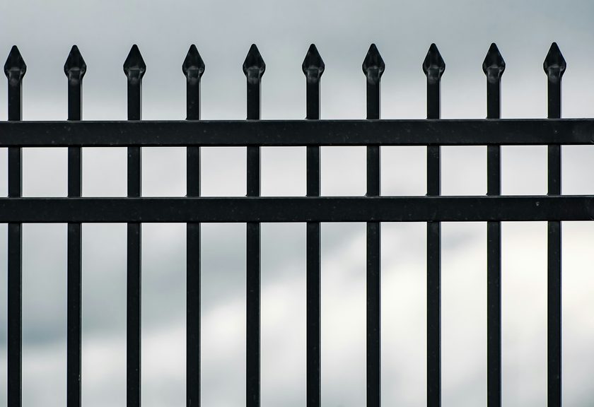 Black metal fence pickets with pointed finials against a gray sky