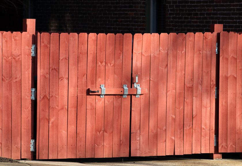 Red-stained wood double gate with metal hinges and a slide bolt